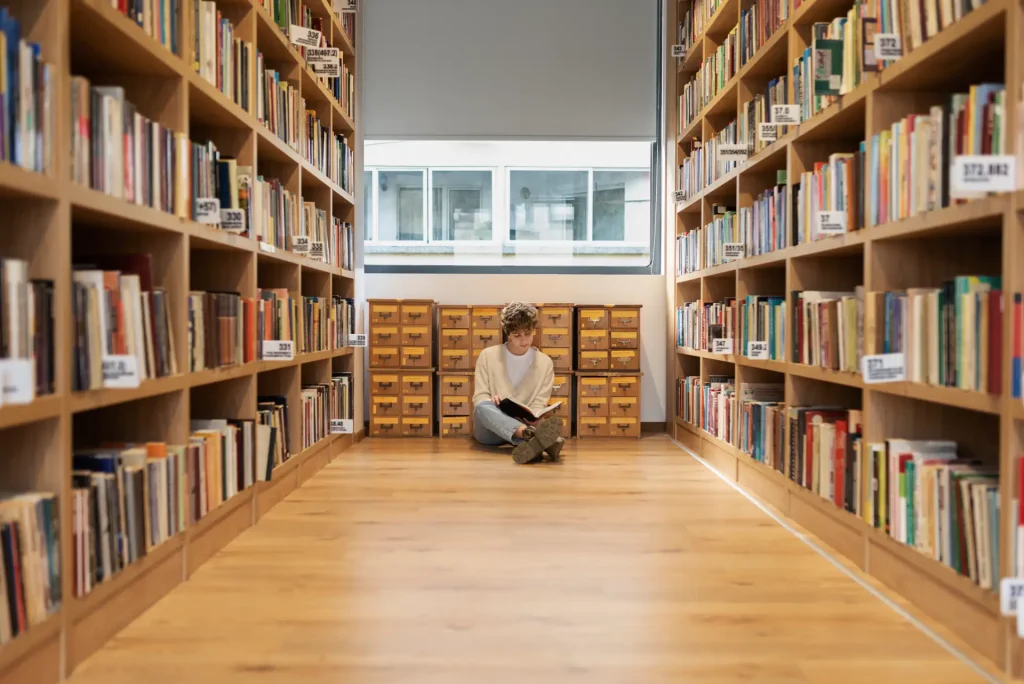 A man wearing headphone sitting on the library's floor to read